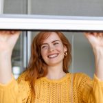 A woman is opening a newly replaced window, loving how it looks and functions.