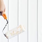 A roller with white paint hanging in front of a freshly painted siding.