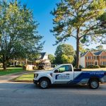 A Southern Exteriors service truck parks along a sunny neighborhood street where local homes are surrounded by mature trees and lush green lawns, showcasing the ideal setting for completing exterior remodeling in the summer.
