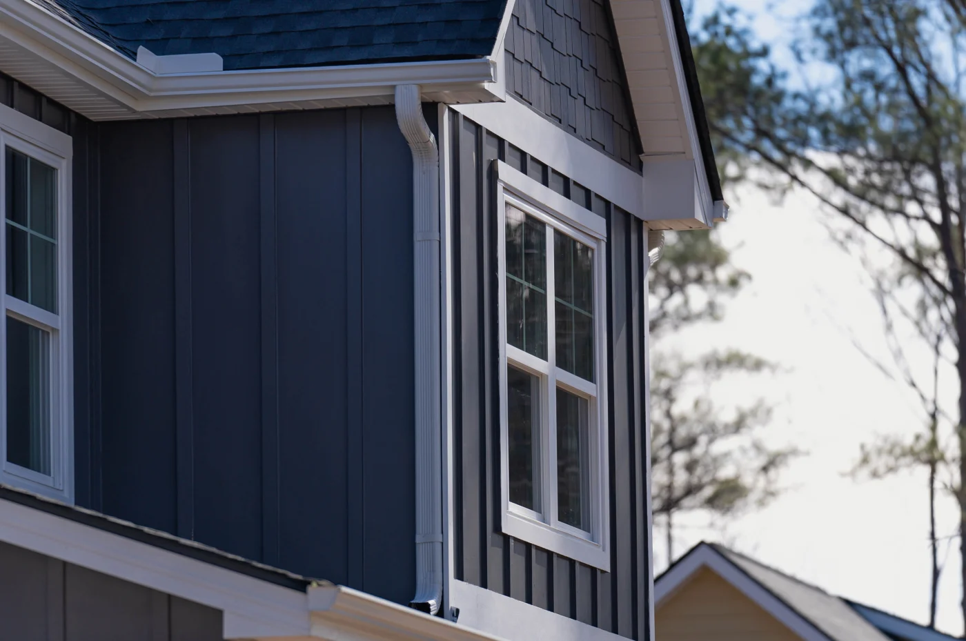 Expert Gutter Services | Columbia, SC | Southern Exteriors A close-up shot highlights clean white seamless gutters and a matching downspout neatly framing dark vertical board and batten siding and a white-trimmed window.