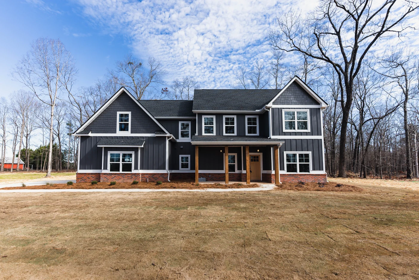 Locally-Trusted Remodeling Contractor | Columbia, SC | Southern Exteriors This sprawling multi-gabled home features striking dark vertical board and batten siding paired with matching shake shingles in the peaks, all beautifully set over a red brick foundation accent and anchored by warm wood porch pillars.